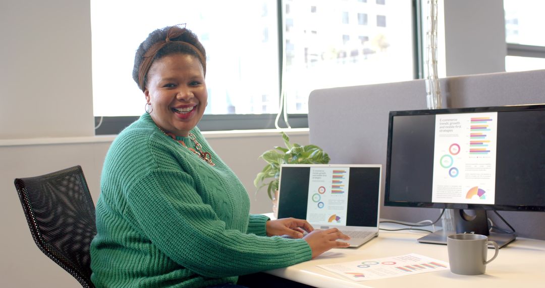 Smiling African American woman typing on laptop with colorful charts on dual screens