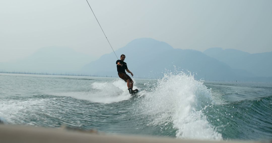 Man Wakeboarding on Lake with Misty Mountains in Background - Free Images, Stock Photos and Pictures on Pikwizard.com