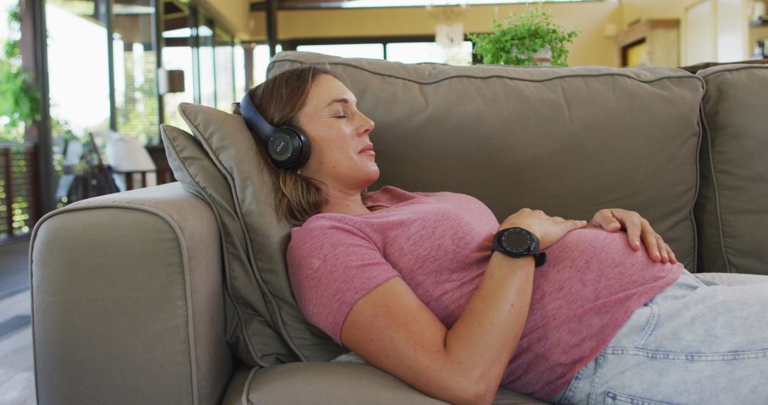 Pregnant Woman Relaxing on Sofa Listening to Music at Home