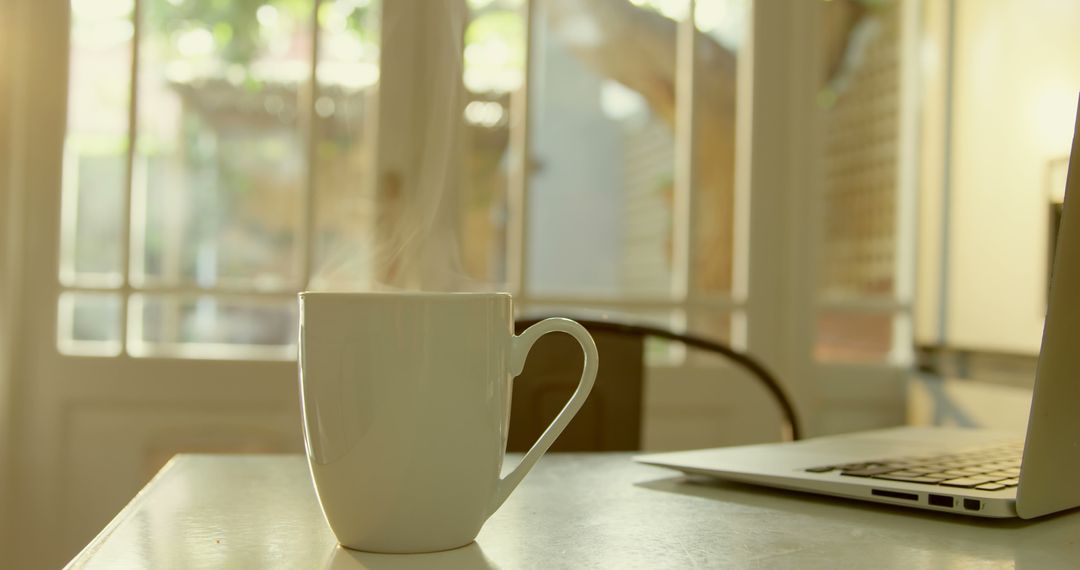 Morning Sunlight on Steaming Coffee Mug Near Laptop in Cozy Home Office - Free Images, Stock Photos and Pictures on Pikwizard.com