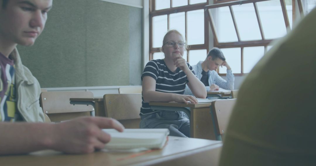 Contemplative Student Wearing Glasses and Striped Tee Resting Chin at Desk with Notebooks