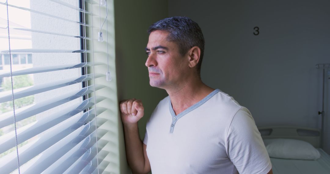 Middle-aged man with graying hair looking out a window with blinds - Free Images, Stock Photos and Pictures on Pikwizard.com