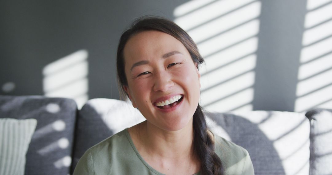 Smiling Woman Sitting on Couch with Light Through Blinds - Free Images, Stock Photos and Pictures on Pikwizard.com