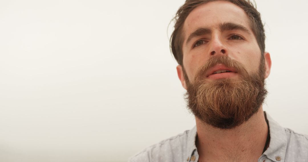 Thoughtful Man with Beard Looking Towards Horizon on Overcast Beach