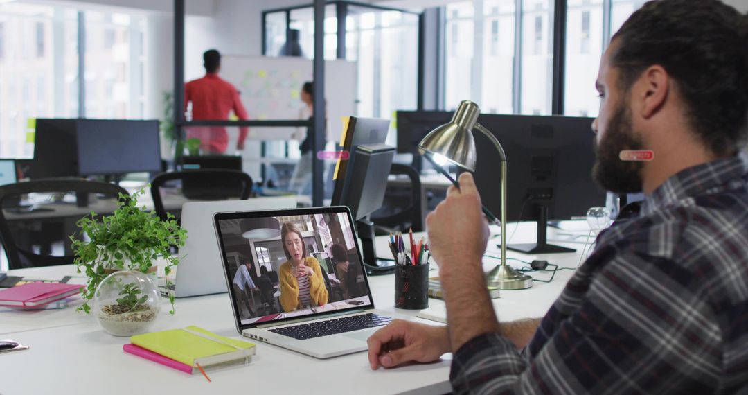 Man Adjusting Desk Lamp During Video Call in Modern Open-Plan Office with Remote Team
