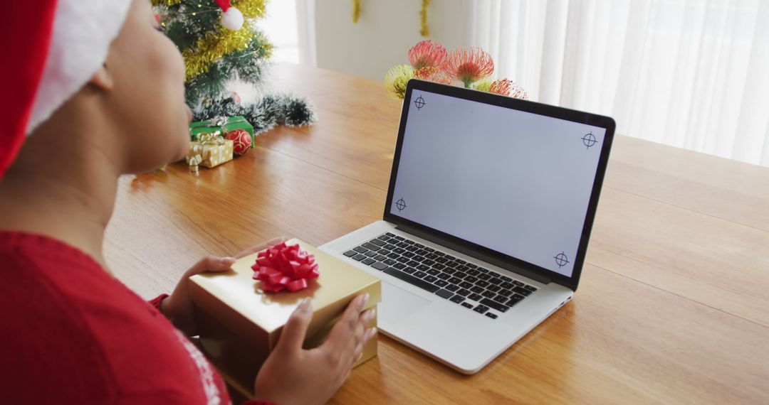 Woman Holding Holiday Gift in Front of Laptop with Christmas Tree in Background - Free Images, Stock Photos and Pictures on Pikwizard.com