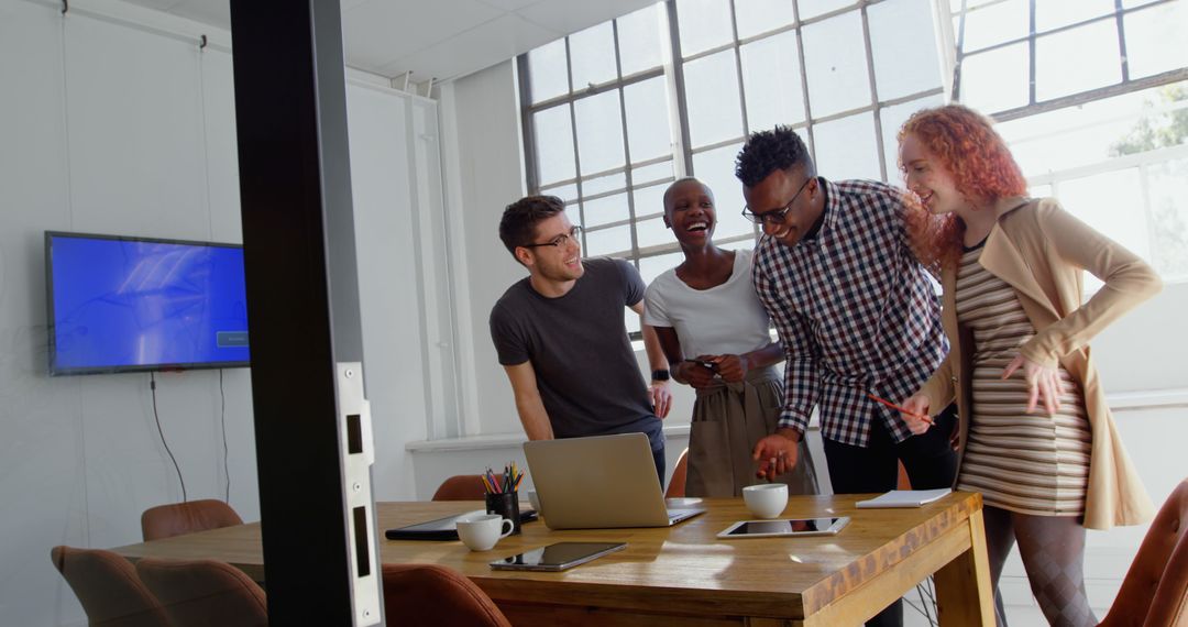 Diverse Team Collaborating and Laughing Over a Laptop in a Bright Office