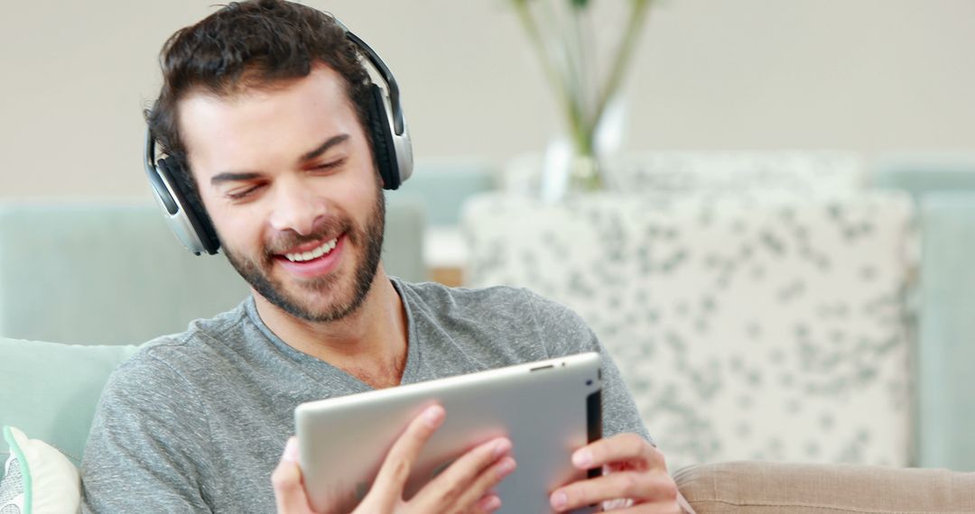 Smiling Young Man with Headphones Using Tablet on Couch - Free Images, Stock Photos and Pictures on Pikwizard.com