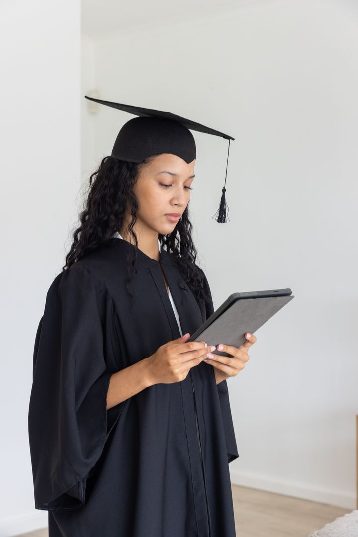 Graduating Student in Cap and Gown Holding Tablet Indoors