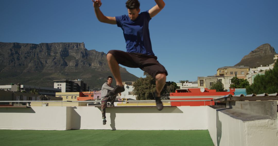 Young men jumping on rooftop with mountain view in background - Free Images, Stock Photos and Pictures on Pikwizard.com