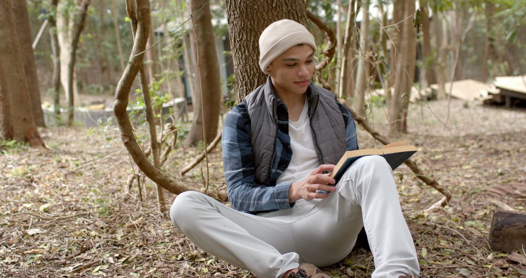 Man Reading Book in Forest Relaxes Against Tree