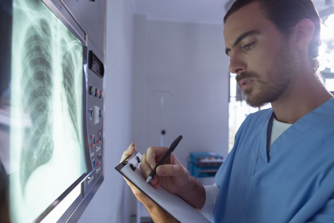 Male Surgeon Examining X-Ray and Writing on Clipboard in Hospital - Free Images, Stock Photos and Pictures on Pikwizard.com