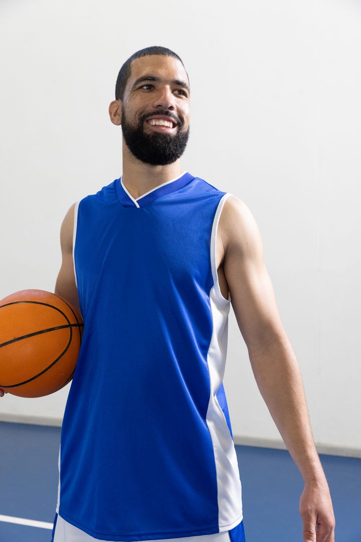 Smiling Basketball Player Holding Ball on Indoor Court