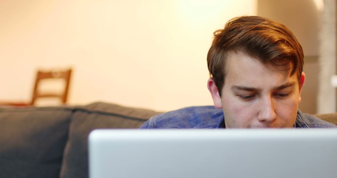 Young Man Focusing on Laptop Screen While Sitting on Couch - Free Images, Stock Photos and Pictures on Pikwizard.com