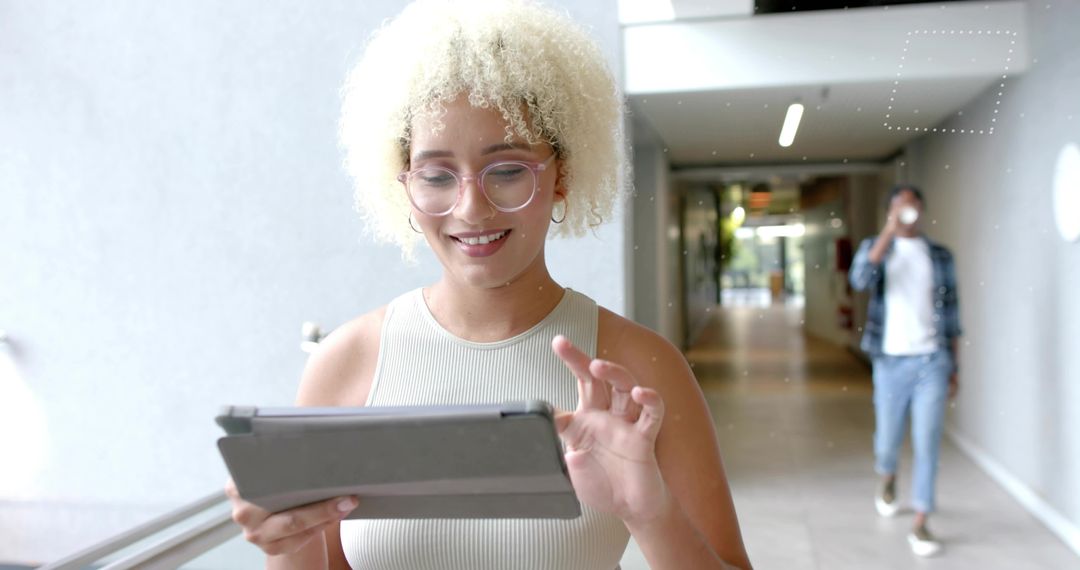 Young professional tapping tablet in bright corridor while colleague sipping coffee