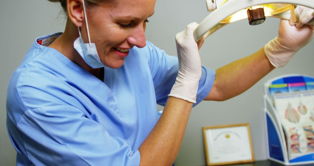 Smiling Dental Professional Adjusting Overhead Light in Clinic - Free Images, Stock Photos and Pictures on Pikwizard.com