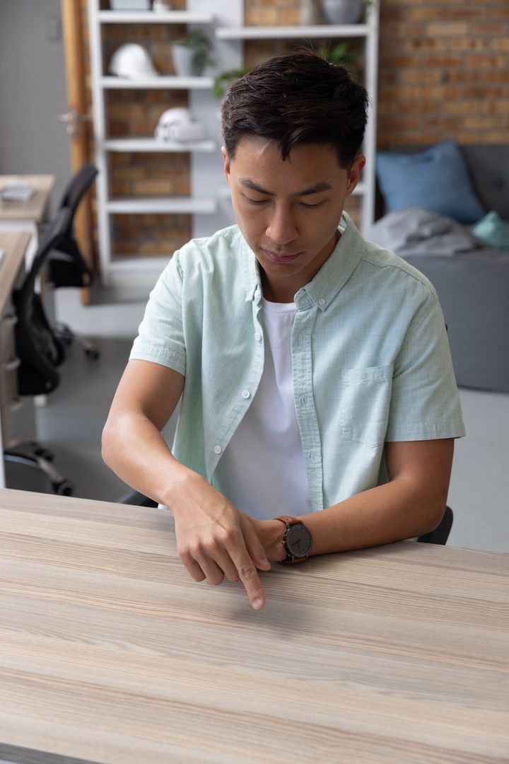 Casual Asian Man Tapping Wood Table in Modern Office Environment