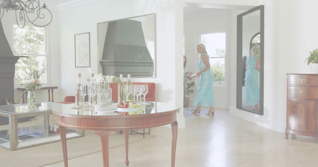 Elegant hostess wearing blue dress carrying tray through bright hallway with round table of wine and