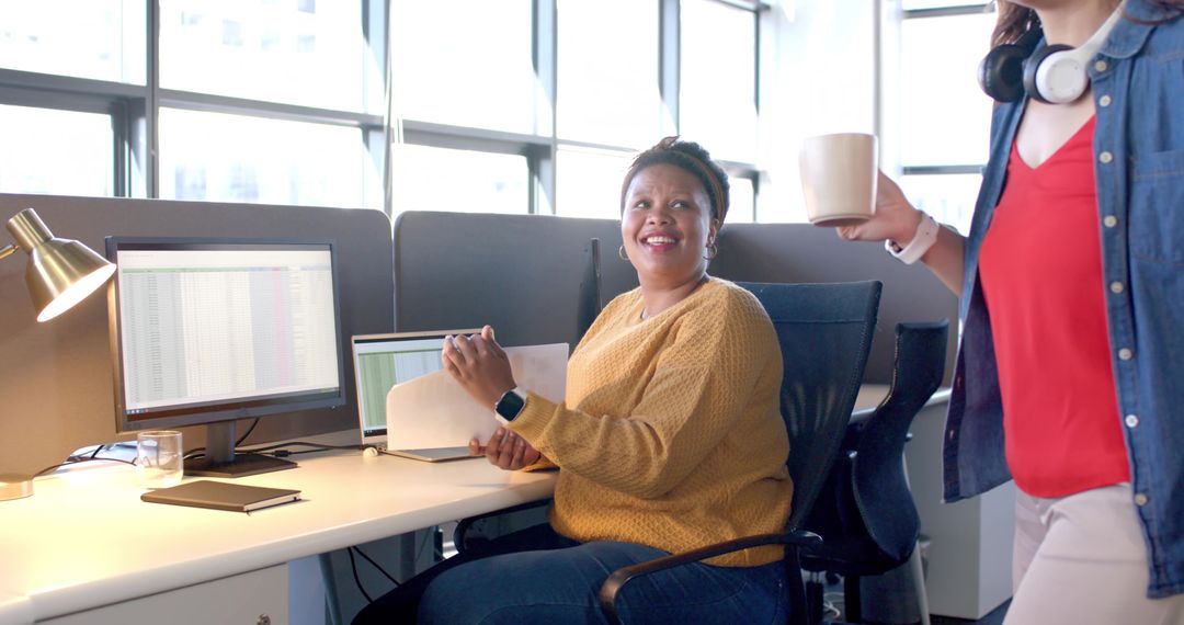 Smiling coworkers collaborating at modern office workstation with laptop, documents, coffee