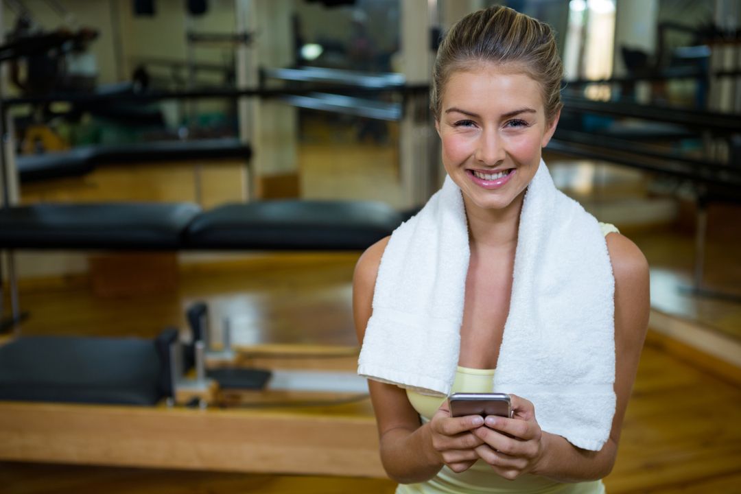 Smiling Woman in Pilates Studio with Smartphone and Towel