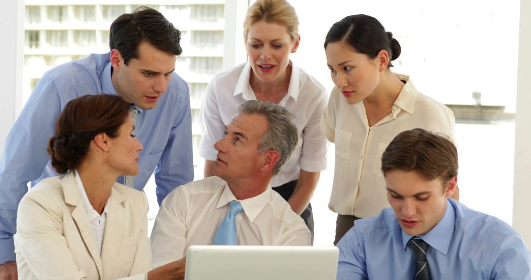 Business team collaborating around laptop in bright office meeting, discussing strategy