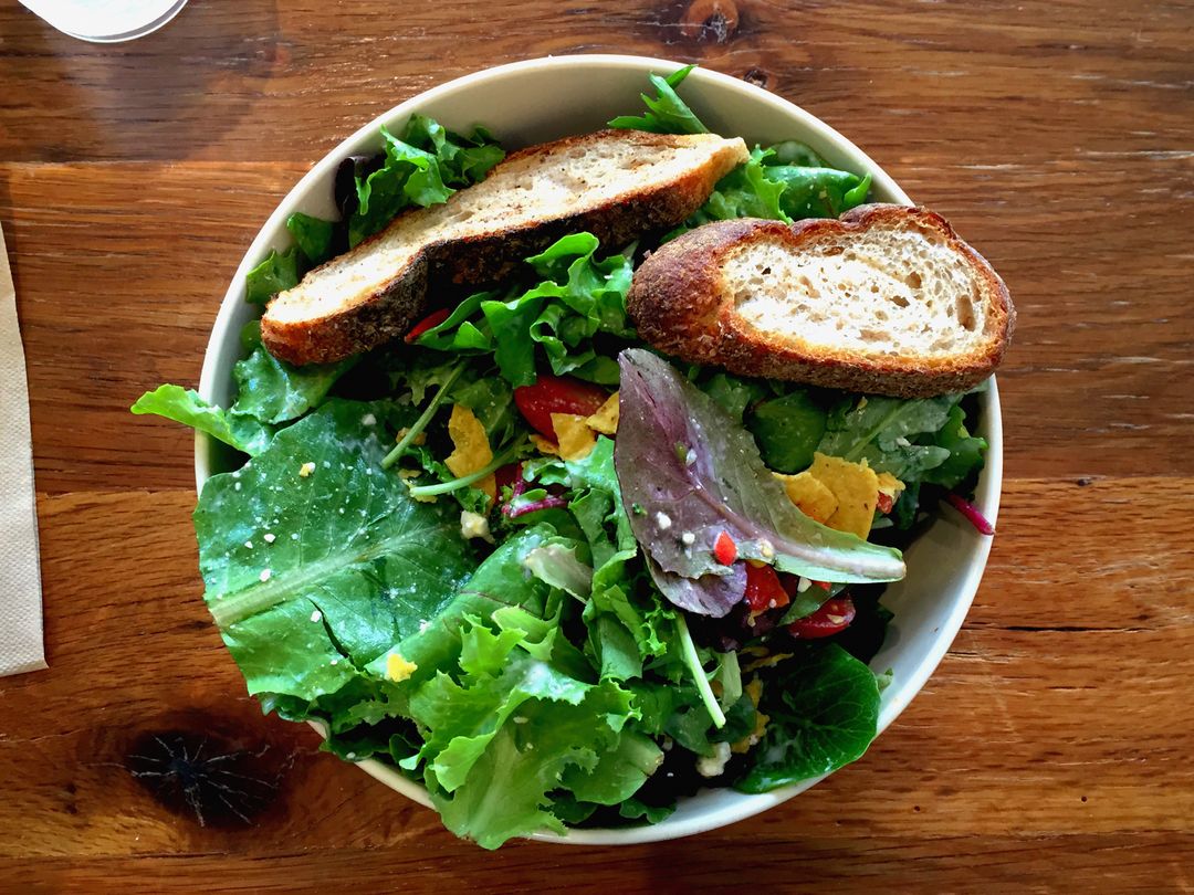 Rustic mixed green salad with toasted sourdough slices on wooden table from top view