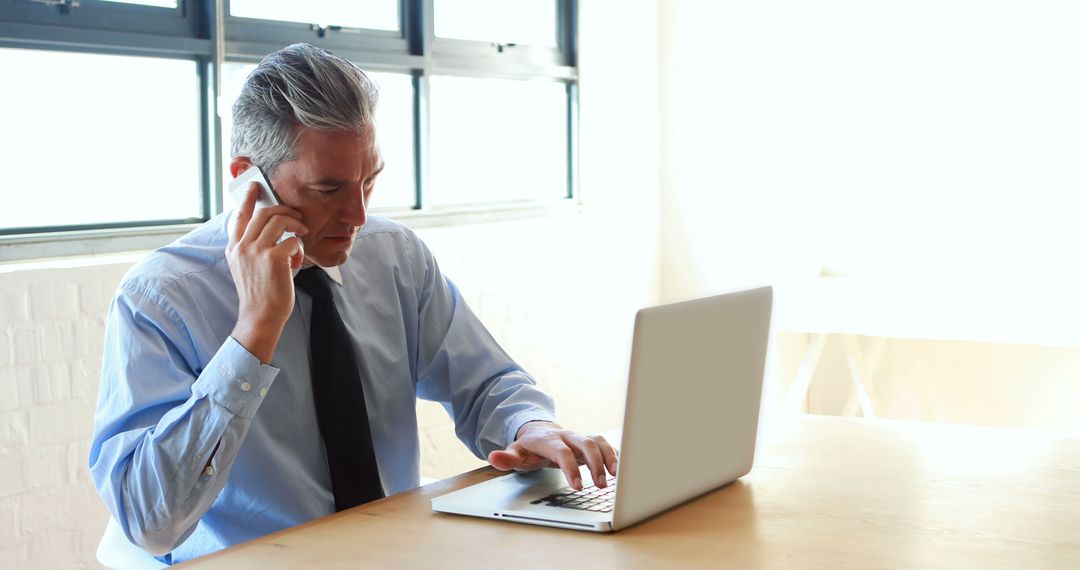 Senior Businessman Talking on Phone and Working on Laptop in Modern Office - Free Images, Stock Photos and Pictures on Pikwizard.com