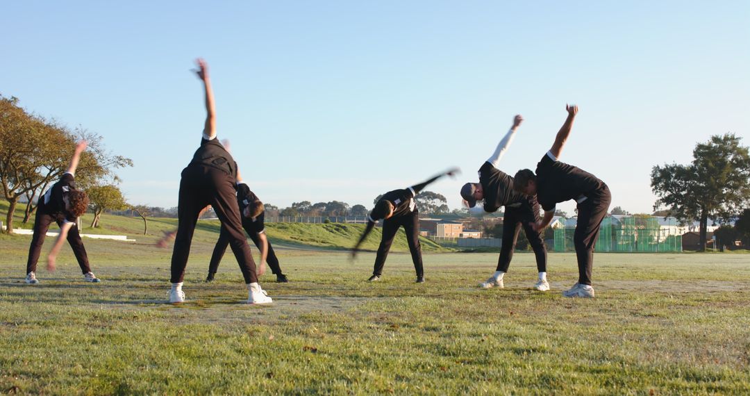Group of Athletes Performing Morning Stretching Routine on Grass Field