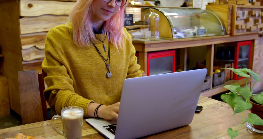 Young woman with pink hair using laptop in cozy coffee shop - Free Images, Stock Photos and Pictures on Pikwizard.com