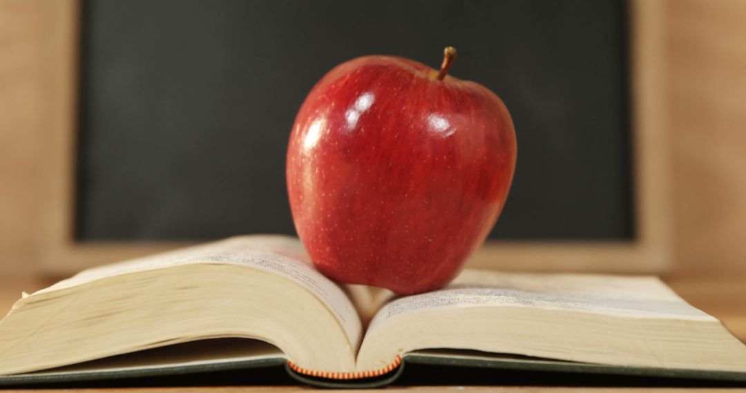 A red apple sits atop an open book in front of a chalkboard, symbolizing education and learning - Free Images, Stock Photos and Pictures on Pikwizard.com
