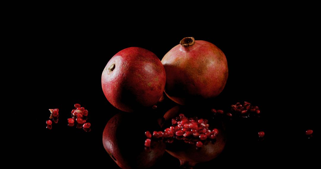 Two Pomegranates Reflecting on Black Surface with Spilled Seeds - Free Images, Stock Photos and Pictures on Pikwizard.com