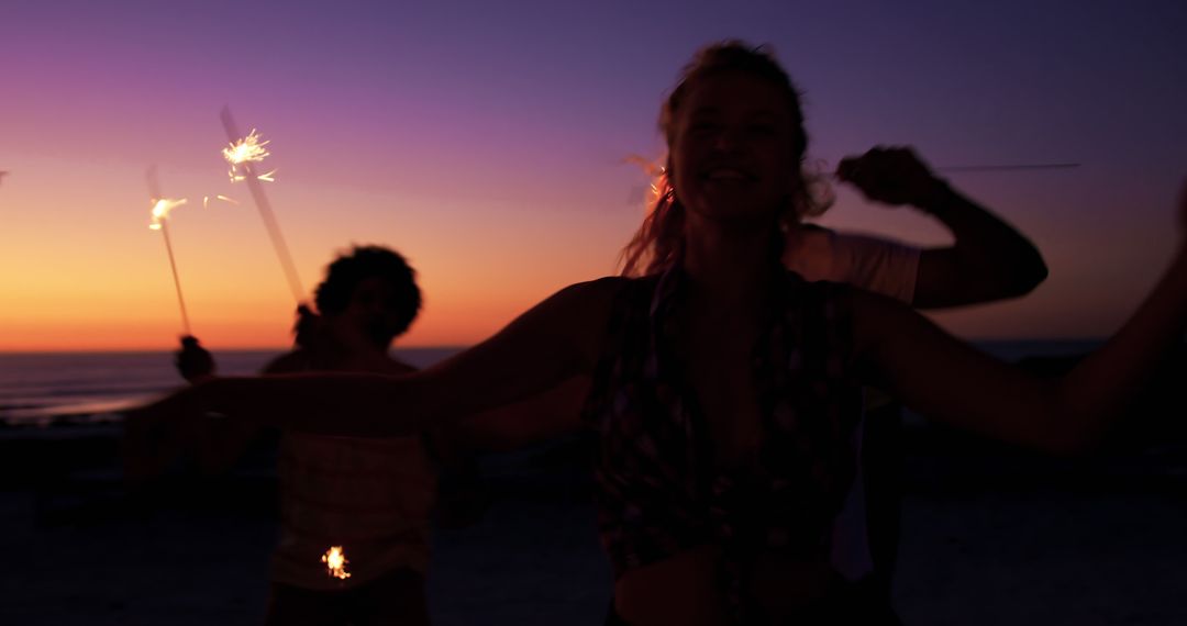 Cheerful Friends Celebrating with Sparklers During Sunset at Beach - Free Images, Stock Photos and Pictures on Pikwizard.com