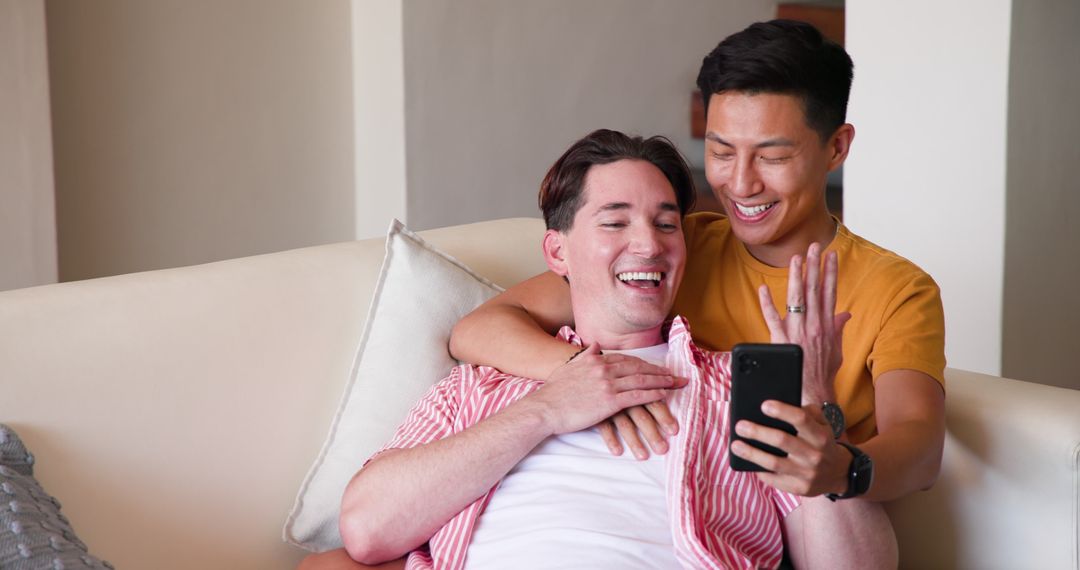 Diverse Gay Couple Smiling on Couch While Using Smartphone