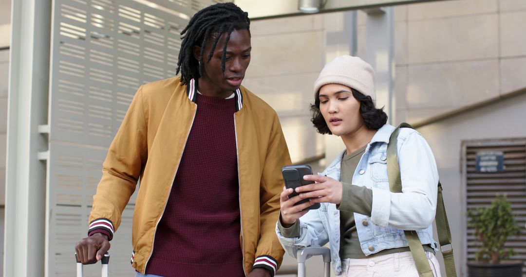 Multicultural travelers checking smartphone at transit hub while wheeling suitcases