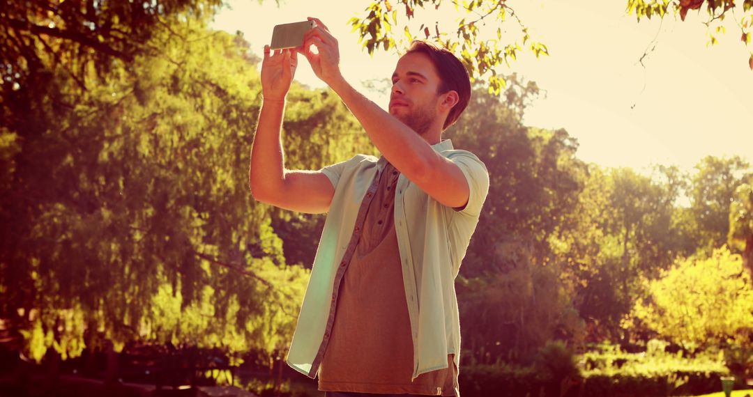 Young Man Taking Smartphone Photos in Sunny Park - Free Images, Stock Photos and Pictures on Pikwizard.com