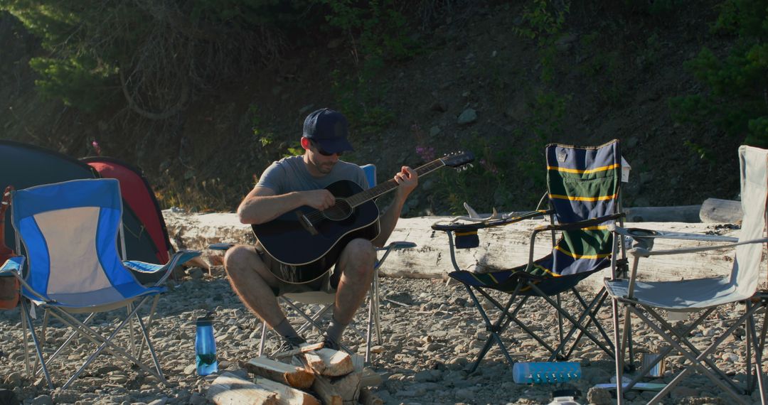 Man Playing Guitar at Camping Site Near River - Free Images, Stock Photos and Pictures on Pikwizard.com