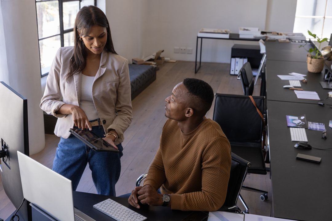 Diverse team collaborating over tablet and desktop in modern open-plan office