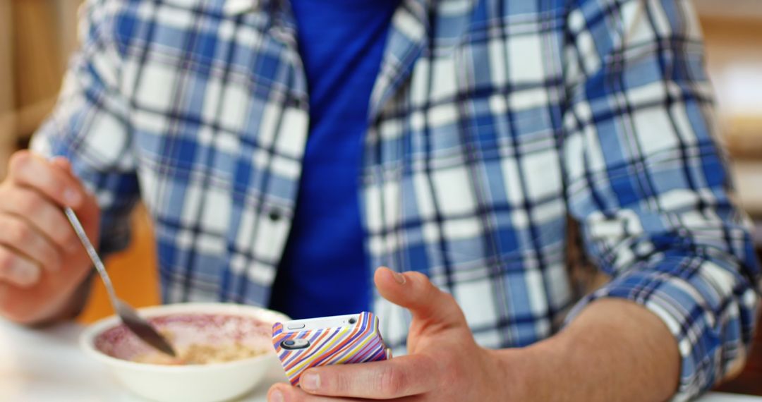 Man Checking Smartphone while Eating Breakfast Cereal - Free Images, Stock Photos and Pictures on Pikwizard.com