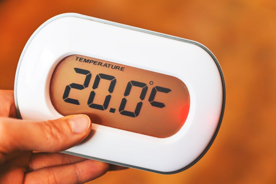 Hand holding digital room thermometer displaying 20.0°C for home comfort and HVAC