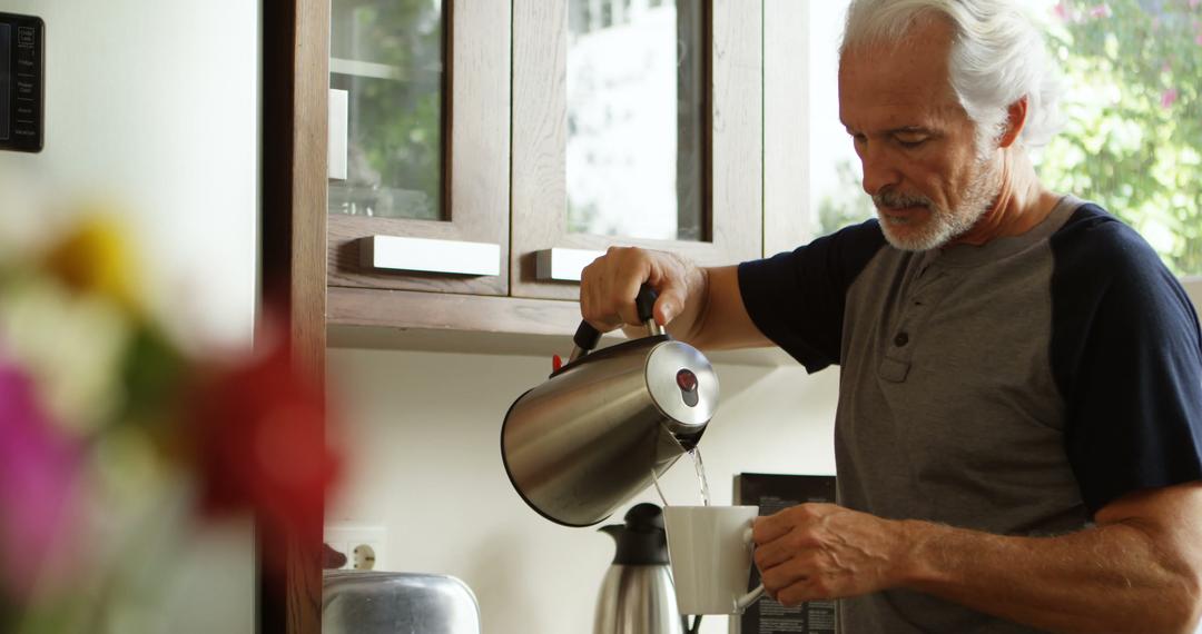 Older man pouring hot water into cup in cozy kitchen - Free Images, Stock Photos and Pictures on Pikwizard.com