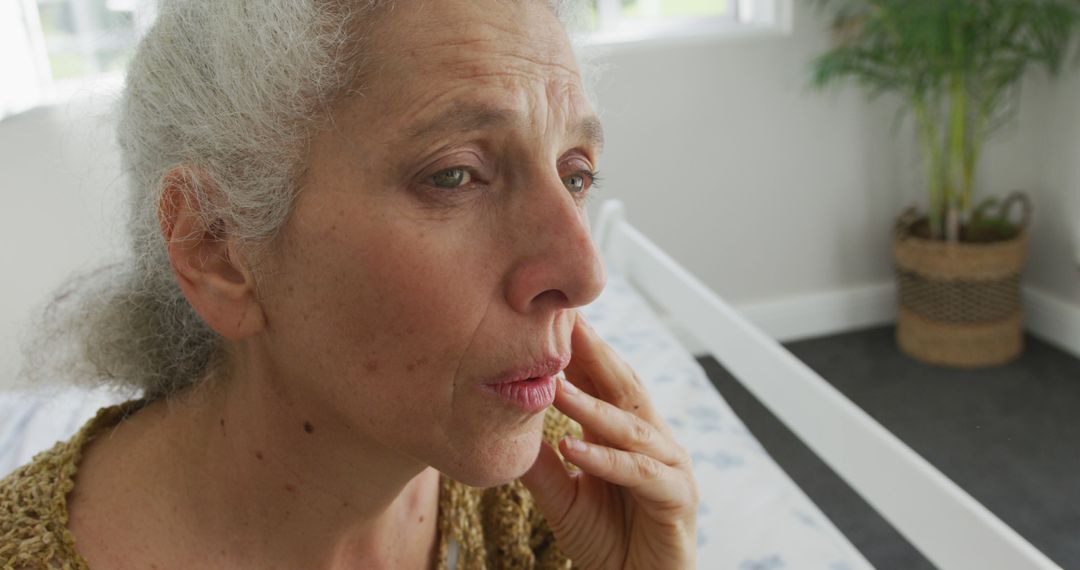 Elderly Woman Lost in Thought Sitting on Bed in Bright Room - Free Images, Stock Photos and Pictures on Pikwizard.com