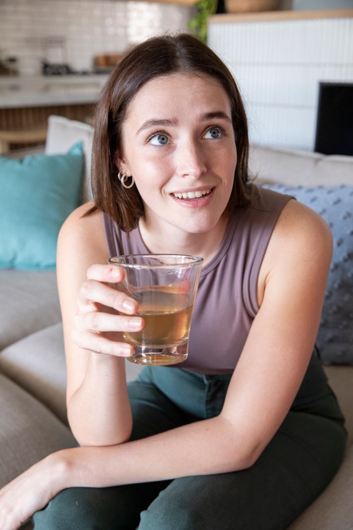 Young Woman Relaxing on Sofa with Refreshing Glass Drink