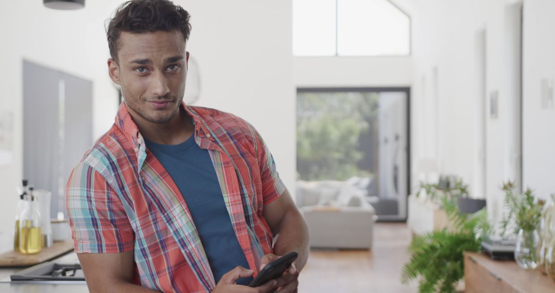 Young Man in Plaid Shirt Smiling and Holding Smartphone in Modern Home - Free Images, Stock Photos and Pictures on Pikwizard.com