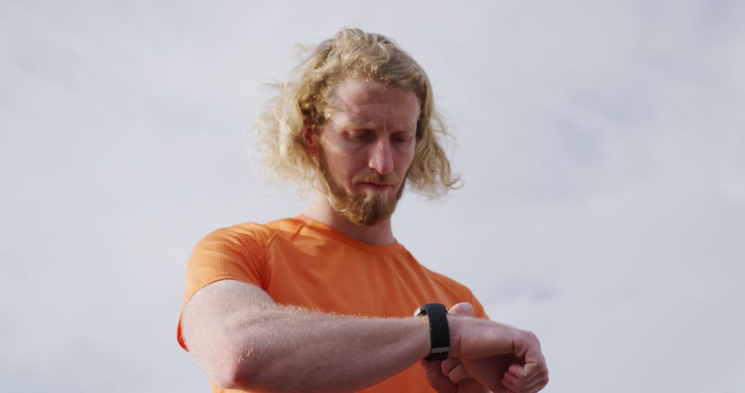 Bearded man checking smartwatch wearing orange T-shirt outdoors - Free Images, Stock Photos and Pictures on Pikwizard.com