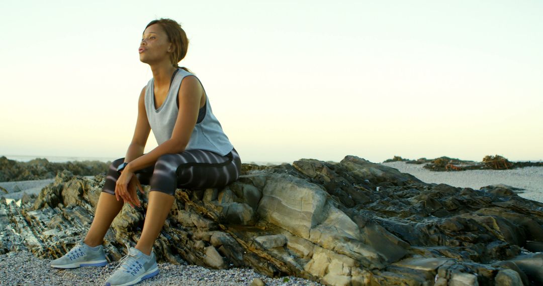 Contemplative Woman Sitting on Rocky Beach During Morning Workout - Free Images, Stock Photos and Pictures on Pikwizard.com