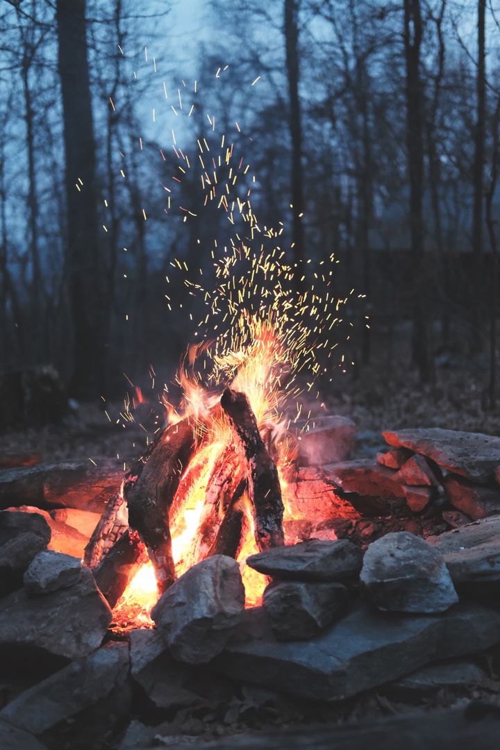 Twilight Campfire with Flying Sparks and Glowing Logs in Rustic Forest Fire Ring