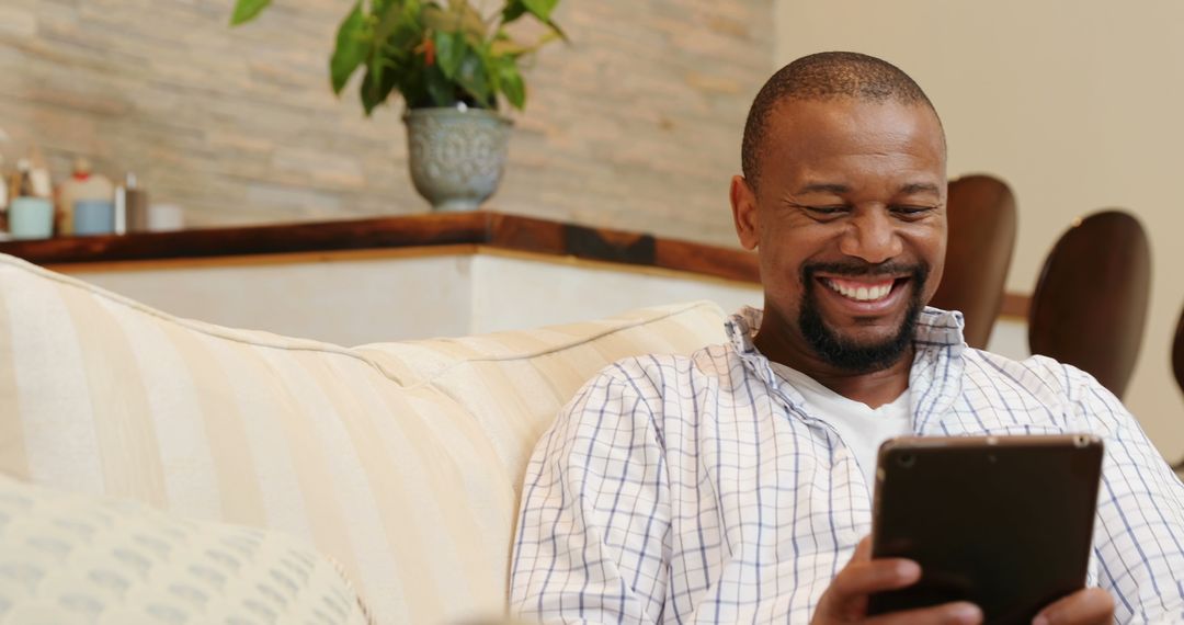 Smiling Man Relaxed on Couch with Digital Tablet in Cozy Living Space