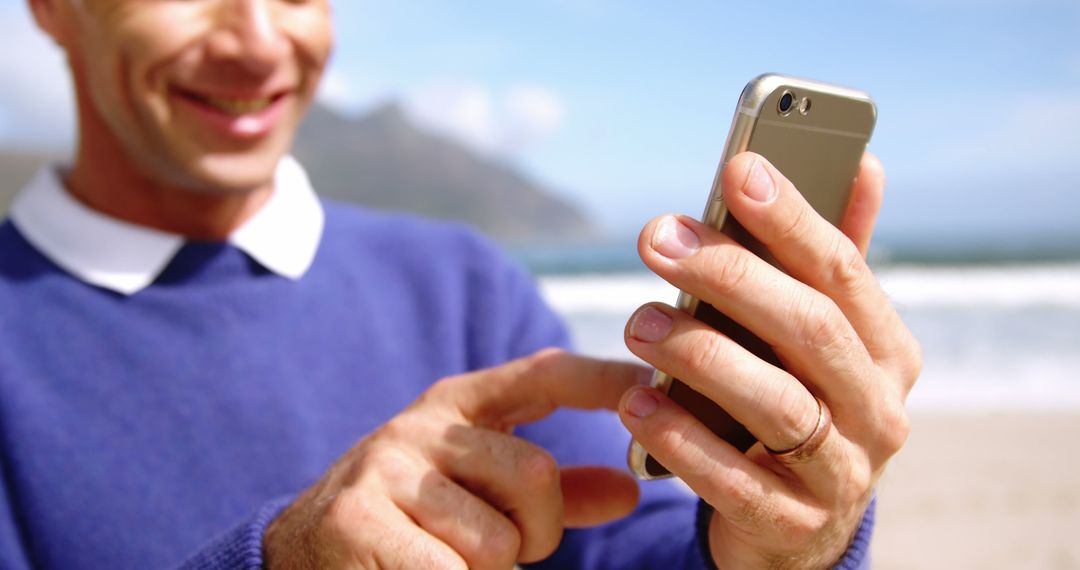 Man holding smartphone smiling by ocean on a sunny day - Free Images, Stock Photos and Pictures on Pikwizard.com