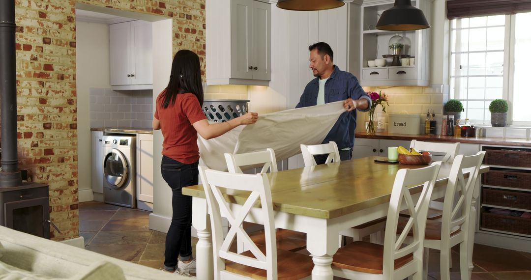 Couple Spreading Tablecloth in Cozy Farmhouse Kitchen Showing Teamwork and Rustic Dining