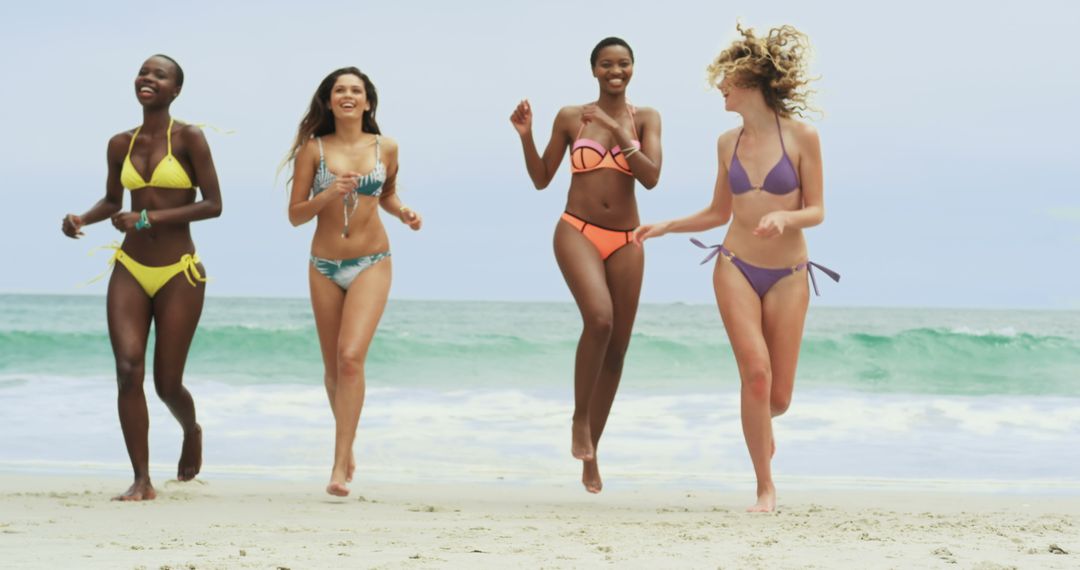 Diverse Friends Running on Sunny Beach in Vibrant Swimwear